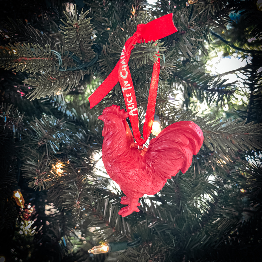 A vibrant red glossy rooster holiday ornament with alice in chains ribbon in a holiday ornament box set